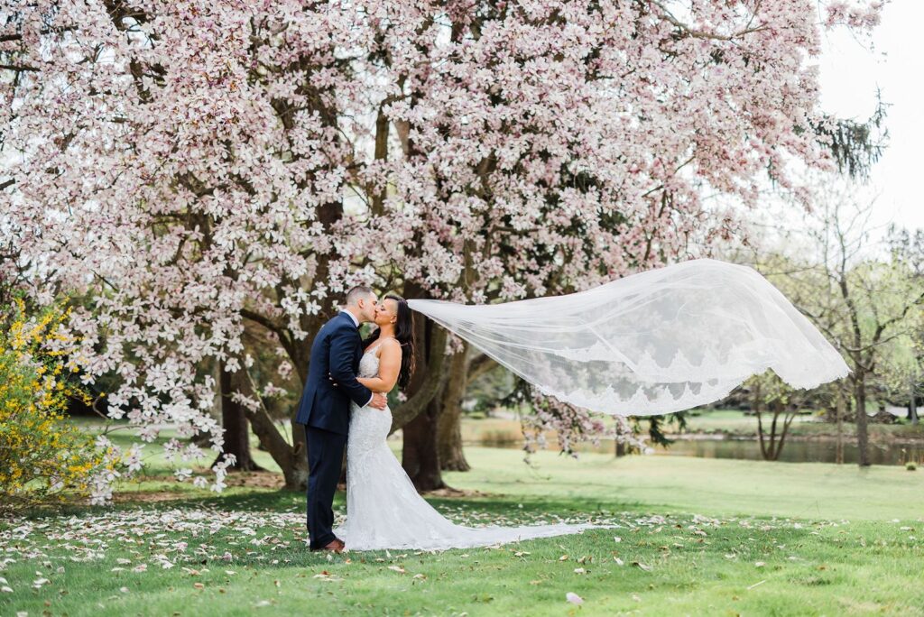 Bride and groom kiss under flower tree at Flowerfield wedding.
