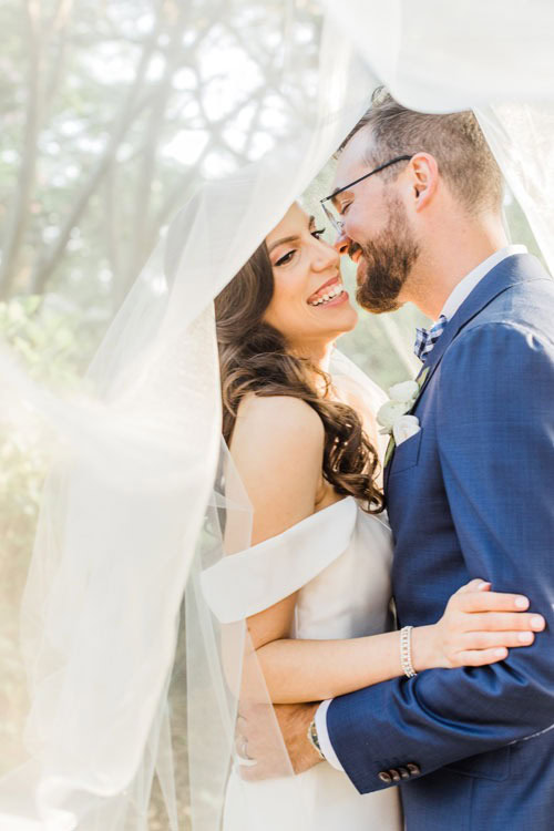Bride and groom pose under veil for Long Island wedding photographer.
